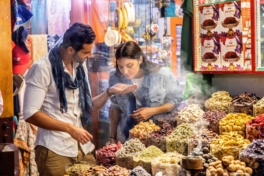 A candid snapshot of a local vendor in Dubai's Spice Souk, surrounded by vibrant displays of spices and herbs, capturing the essence of the city's bustling markets.